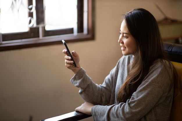 Closeup retrato jovem asiática linda mulher sorrindo e usando um smartphone para negócios ou compras online em uma cafeteria