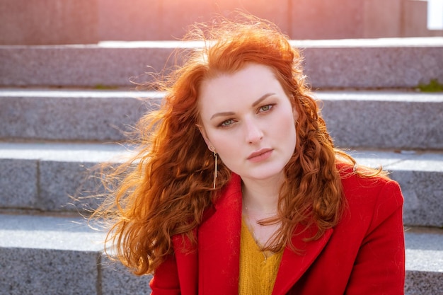 Closeup retrato jovem mulher caucasiana com cabelo ruivo encaracolado em casaco vermelho ao vento