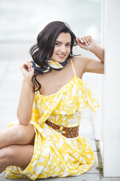 Closeup retrato de joven atractiva en vestido amarillo. Ocio de verano. Hermosa mujer elegante caminando por la ciudad. Mujer junto a la fuente.