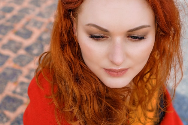 Closeup retrato joven mujer caucásica con pelo rizado rojo en un abrigo rojo