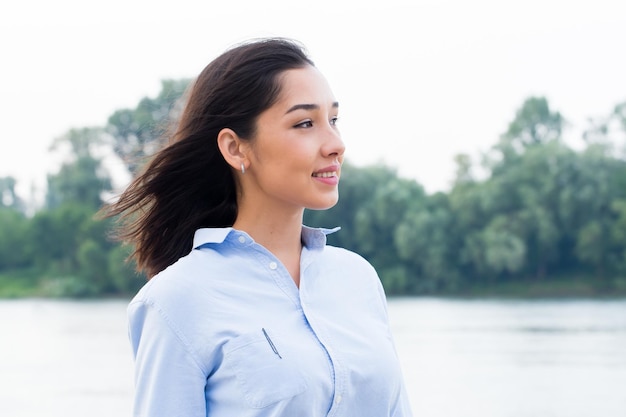 Closeup retrato lateral de hermosa mujer morena asiática con camisa azul sobre fondo de naturaleza
