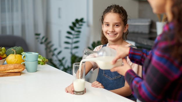 Closeup retrato de una mamá vierte su linda hija sonriente leche para el desayuno