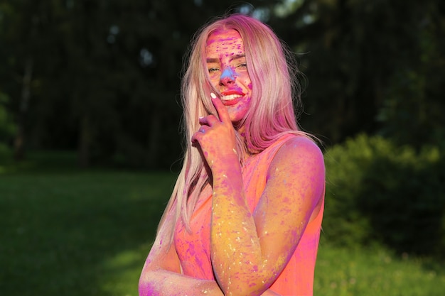 Closeup retrato de modelo alegre posando cubierto con una colorida pintura seca en el parque