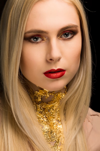 Foto closeup retrato de modelo rubia con lámina de oro en el cuello posando en el estudio