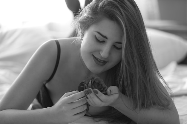 Foto closeup retrato monocromo linda mujer acostada en la cama y sosteniendo rosa