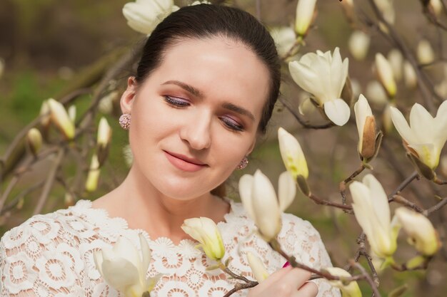 Closeup retrato de mujer bonita morena con maquillaje nude posando cerca de las flores de magnolia en flor