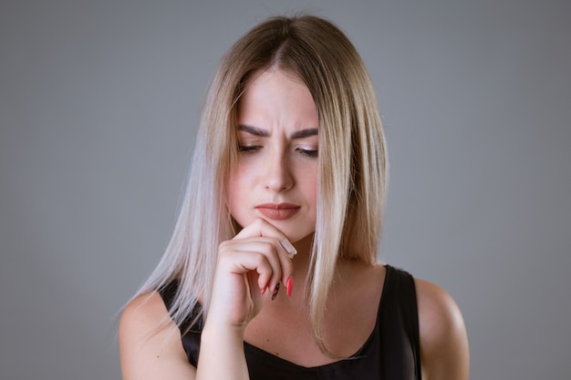 Closeup retrato de una mujer con el ceño fruncido en una pared clara mujer rubia en camiseta negra