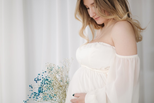 Closeup retrato de mujer embarazada en vestido blanco puso su mano sobre el vientre y esperando que el bebé se mueva