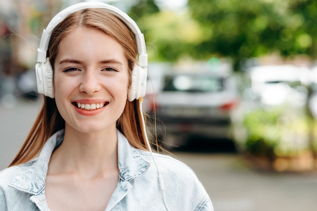 Closeup retrato de mujer feliz en auriculares al aire libre. Fondo borroso