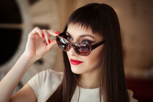 Closeup retrato de mujer hermosa de moda con gafas de sol con manicura de esmalte de gel rojo. Maquillaje modelo.