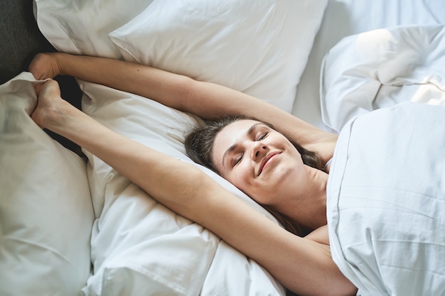 Closeup retrato de una mujer joven linda sonriente que se estira en la cama por la mañana