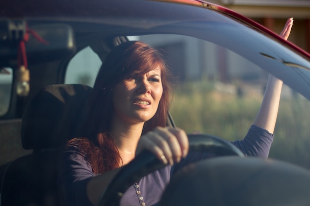 Closeup retrato, mujer sentada joven enojada cabreada por los conductores frente a ella y gesticulando con las manos. Concepto de atasco de tráfico de rabia en la carretera