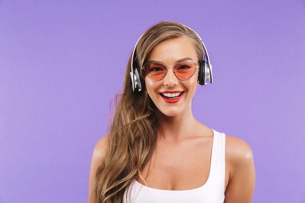 Closeup retrato de mujer sonriente en ropa de verano y gafas de sol escuchando música con auriculares inalámbricos