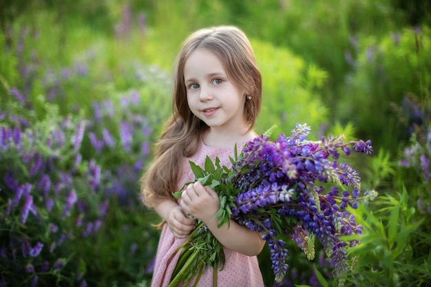 Closeup retrato de niña sonriente con ramo de altramuces niño en pradera de verano