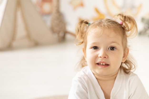 Closeup retrato niño niña rubia con ojos azules sonriendo en la habitación de los niños