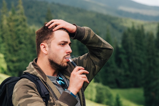 Closeup retrato de un turista masculino adulto fuma un cigarrillo electrónico y mira hacia otro lado