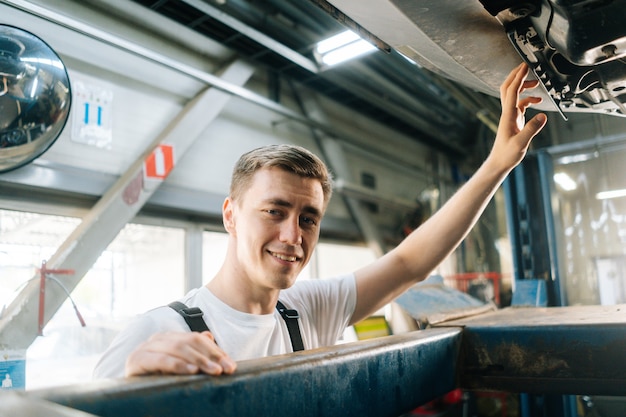 Closeup rosto sorridente e bonito mecânico de automóveis masculino profissional de uniforme em pé no carro