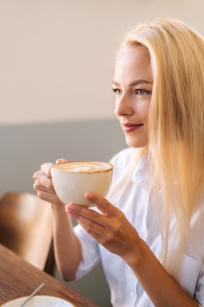 Closeup rosto sorridente jovem loira segurando uma xícara de café com leite quente com linda