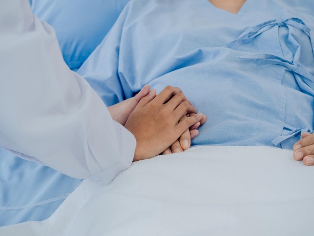 Closeup Ärztin im weißen Anzug hält sich an der Hand der älteren Seniorin in hellblauem Kleid mit einem Kochsalzschlauch, der auf dem Krankenhausbett liegt und das Patientenkonzept fördert