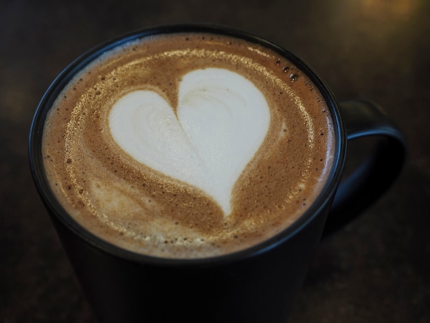 Foto closeup seletivo com foco na arte com leite em forma de coração na xícara de café, café com leite quente na mesa