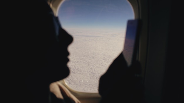 Closeup Silhouette Frau sitzt in der Nähe von Flugzeugfenster mit Handy während des Fluges
