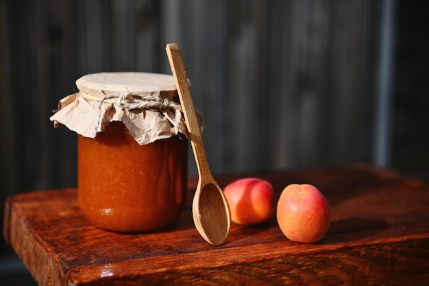 Closeup Stillleben Glas mit hausgemachter Marmelade reife readytoeat rote sonnige Aprikosen und Holzlöffel auf rustikaler Holzoberfläche