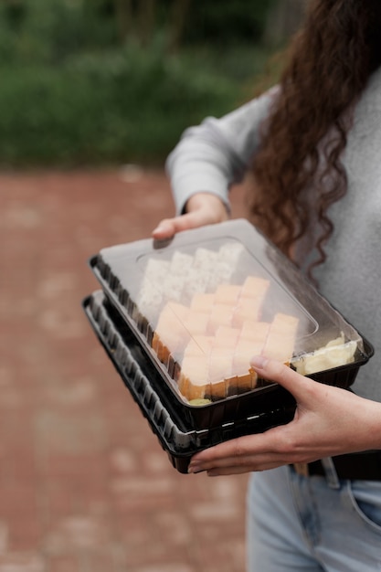 Closeup sushi en caja servicio en línea de entrega de alimentos saludables. La niña tiene 2 juegos de sushi en las manos. Rollos de cocina japonesa, salsa de soja, wasabi.