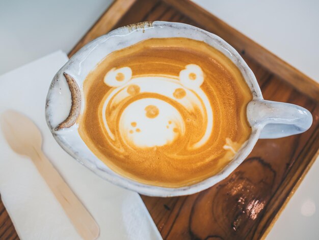 Closeup Teddybär Latte Art Kaffee in handgefertigter Keramiktasse auf Holztablett auf weißem Hintergrund