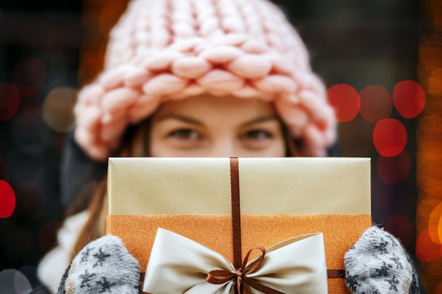 Closeup tiro de alegre menina loira segurando uma caixa de presente. Fundo desfocado bokeh. Espaço para texto