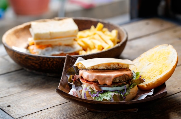 Closeup tiro de delicioso saboroso delicioso café da manhã caseiro suculento hambúrguer de carne grelhada com alface vegetal fatiado repolho tomate cebola e molho picante derretido em tigela de madeira na mesa de madeira