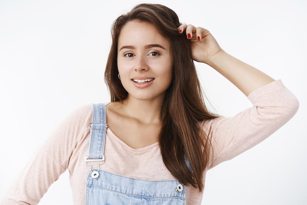 Closeup tiro de glamour encantador menina feminina tocando cabelo e sorrindo encantado e sonhador para a câmera com dentes brancos em pé sensual e feliz posando sobre fundo cinza