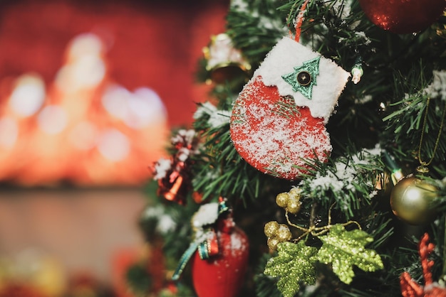 Closeup tiro de meia decorada pendurada no galho de pinheiro da árvore de Natal com uma bola e vários enfeites de Natal decoração cobrir com flocos de neve e desfocar o fundo da chama de fogo na lareira.