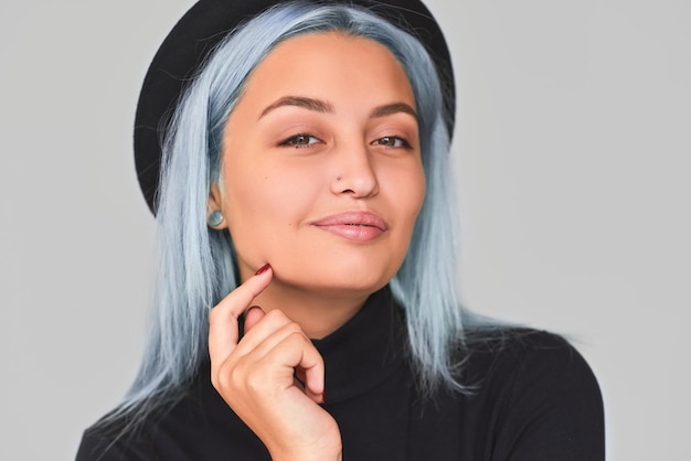 Closeup tiro de mulher adolescente alegre e encantadora com cabelo azul, vestindo roupas pretas e chapéu sorrindo Bonita fêmea positiva posando em fundo cinza claro Peopla e conceito de estilo de vida