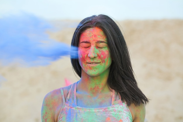 Closeup tiro de uma jovem modelo bronzeada e atraente se divertindo em uma nuvem de tinta azul seca Holi