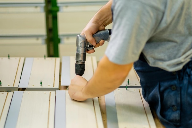 Closeup Tischler bohrt Holzplatte mit Bohrmaschine im Holzsägewerk Professioneller Tischler bohrt in der Holzmöbelproduktion Tischlerei Möbelmontage in einer Möbelfabrik