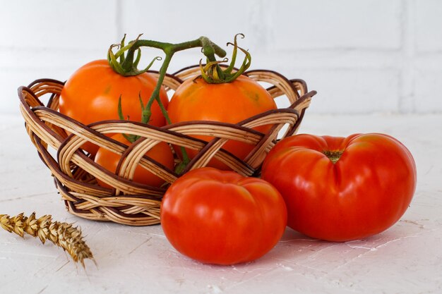 Closeup tomates rojos y amarillos maduros en una cesta de mimbre una espiga de trigo