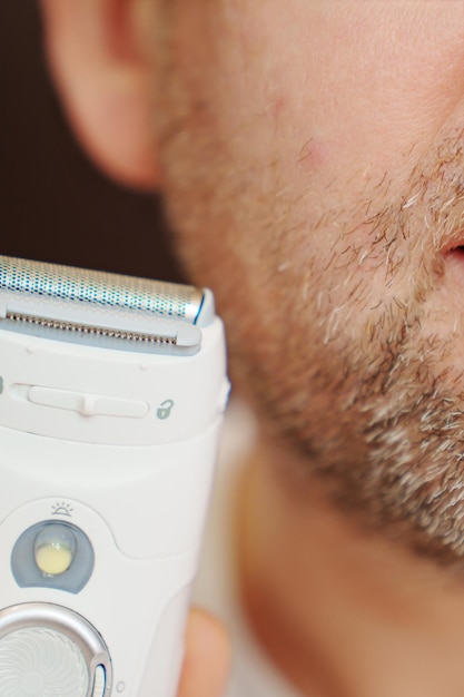 Closeup um homem com cerdas segurando um aparador de barbear elétrico