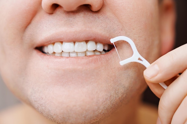Closeup um homem escova os dentes palito de plástico com fio dental