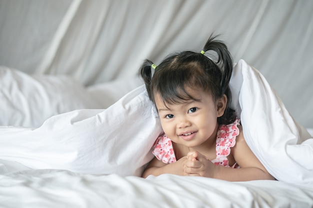 Closeup uma garotinha mentira na cama sob o cobertor com sorriso rosto de manhã