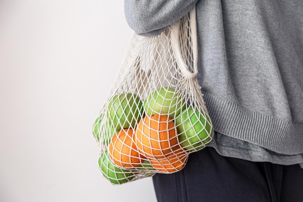 Foto closeup uma mulher segura um saco de cordas com maçãs e laranjas