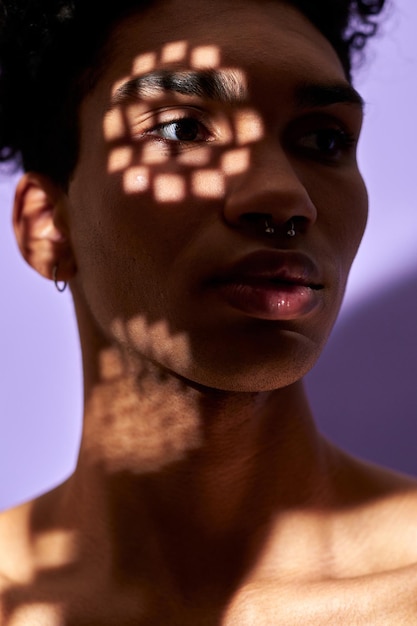 Closeup vertical vertical de la cara del hombre joven latino en textura sombras luces en el ojo de género trans
