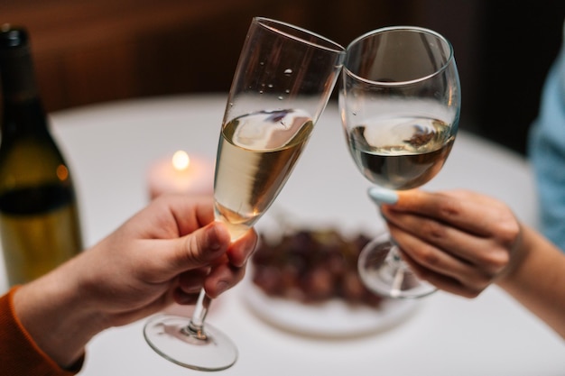 Closeup vista de alto ângulo de um casal feliz tilintando copos com vinho na mesa com velas no quarto escuro aconchegante