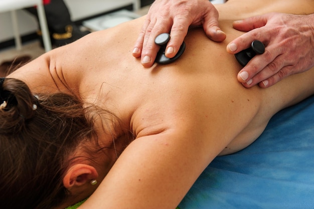 Closeup vista de massagista masculino massageando costas e omoplatas de mulher deitada na mesa de massagem no salão spa Mulher jovem e bonita com pele perfeita recebendo massagem relaxante