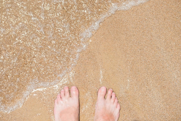 Closeup vista de pés humanos nus no fundo da praia de areia. conceito de férias de verão