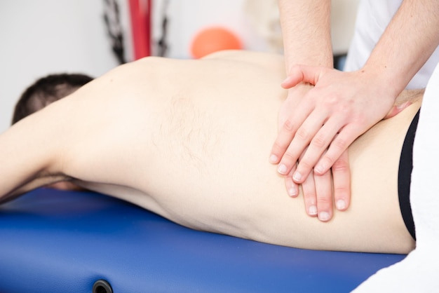 Closeup vista de um fisioterapeuta massageando as costas e a cintura de um paciente.