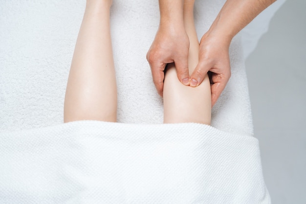 Closeup vista superior de massagista massageando a parte inferior da perna de uma jovem deitada na mesa de massagem