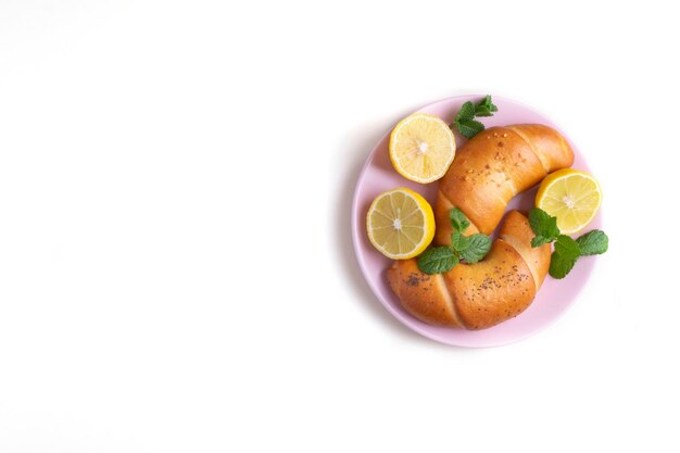 Closeup vista superior em uma superfície branca dois bagels de pastelaria estão em um prato de cerâmica rosa com metades de limão e folhas de hortelã Foco seletivo Espaço para cópia