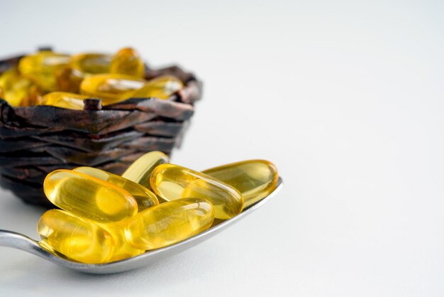 Closeup von Fischöl-Kapseln in einem Löffel und Korb auf weißem Hintergrund Omega-3-Kapseln natürliche Vitamine