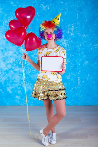 Clown feliz conceito de feriados Uma jovem alegre em um terno de palhaço posando na frente de uma câmera em um fundo azul conceito de Dia dos tolos de 1o de abril aniversário