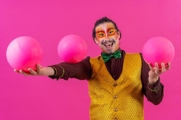 Clown mit weißem Gesichts-Make-up auf rosafarbenem Hintergrund, der mit Bällen jongliert